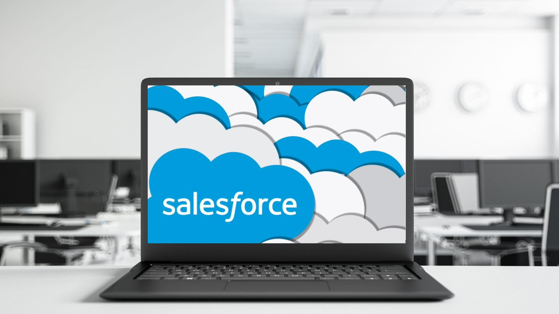 Laptop on an office desk displaying the Salesforce logo with cloud graphics on the screen.